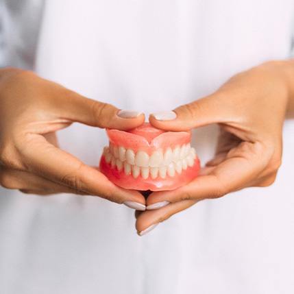 Two hands holding complete set of dentures