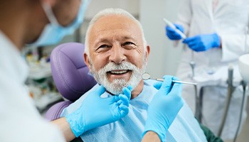 Older man in dental chair smiling and provider before dental exam