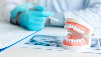 Blue-gloved hands at desktop with X-rays, model teeth, and treatment plan