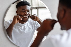 Man smiling while flossing in bathroom