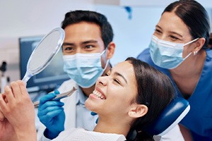 Patient smiling at reflection with dentist and dental hygienist