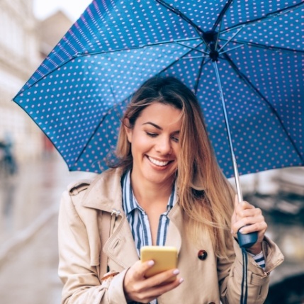 Woman with umbrella outdoors looking at dental insurance information on her phone