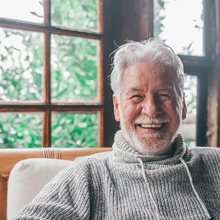 Older man wearing gray sweater and smiling with dentures