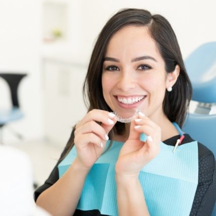 Smiling woman holding aligner for Invisalign in Catonsville