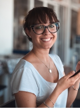 Young woman with glasses smiling while holding cell phone