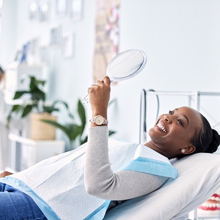 Woman smiling at reflection in handheld mirror at dental office