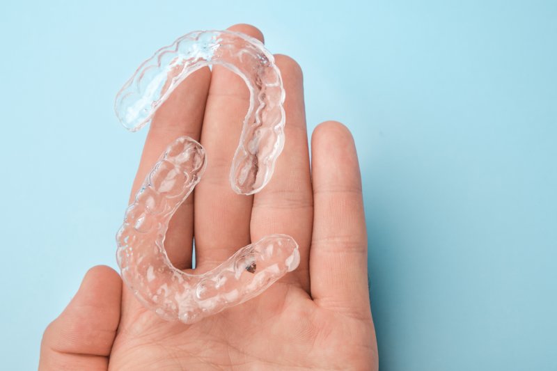 Two clear aligners resting on a person's palm over a light blue background
