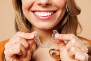 Woman smiling and holding clear aligner in foreground.