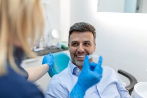 Middle-aged man smiling in dentist’s chair while dentist holds clear aligner.
