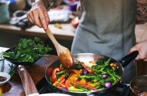 Person cooking vegetables in skillet on stovetop.